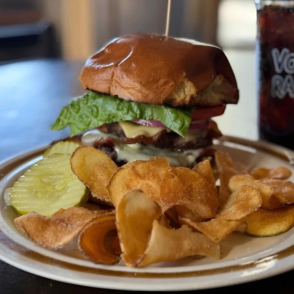 Cheeseburger with lettuce, bacon, pickles, and onion rings served with a dark soft drink.